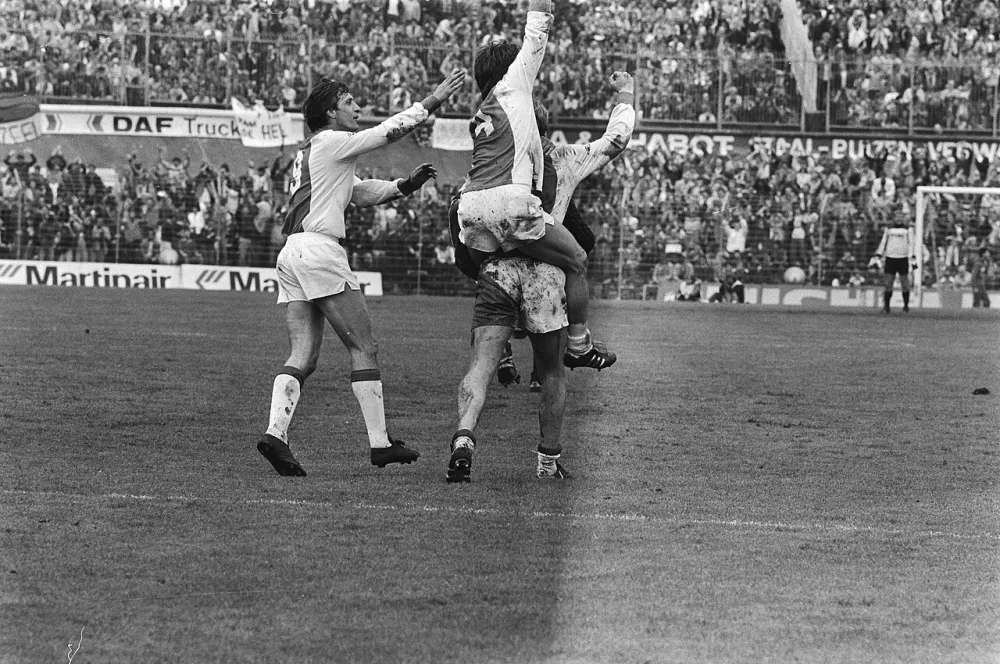 Vreugde na een tweede doelpunt van Ajax; Johan Cruijff feliciteert Sören Lerby die een juichende Boeve op zijn rug heeft. Foto: Rob Bogaerts / Anefo, Nationaal Archief (CC0).